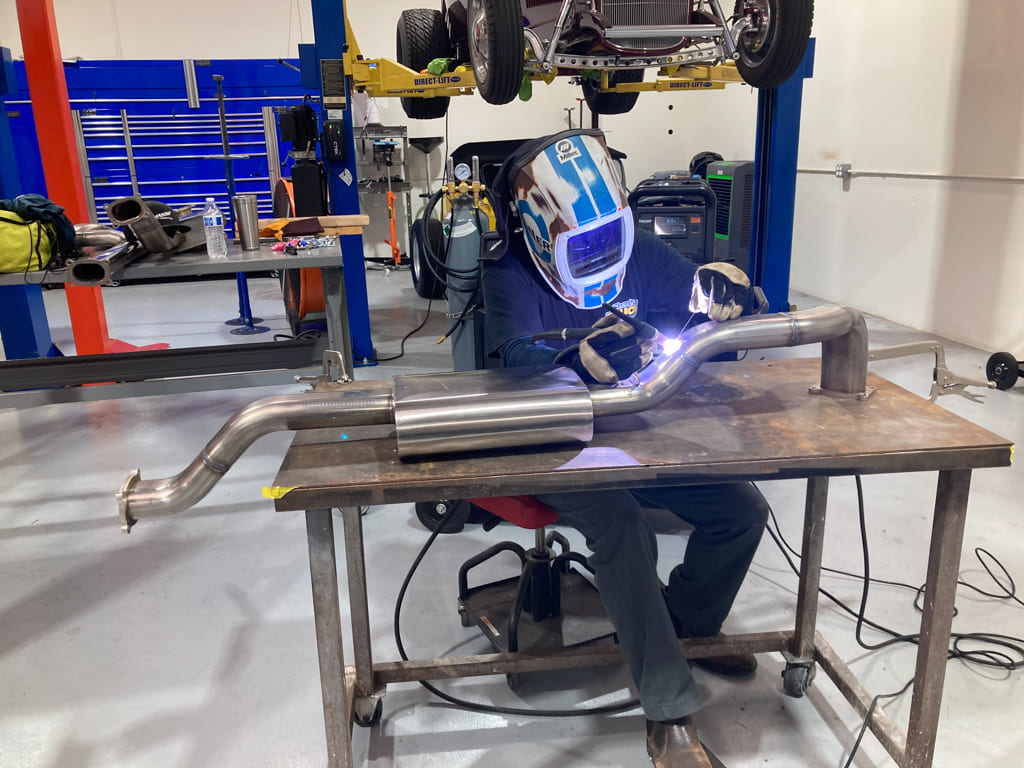 Avid technician TIG-welding a custom mandrel-bent exhaust on the fab table