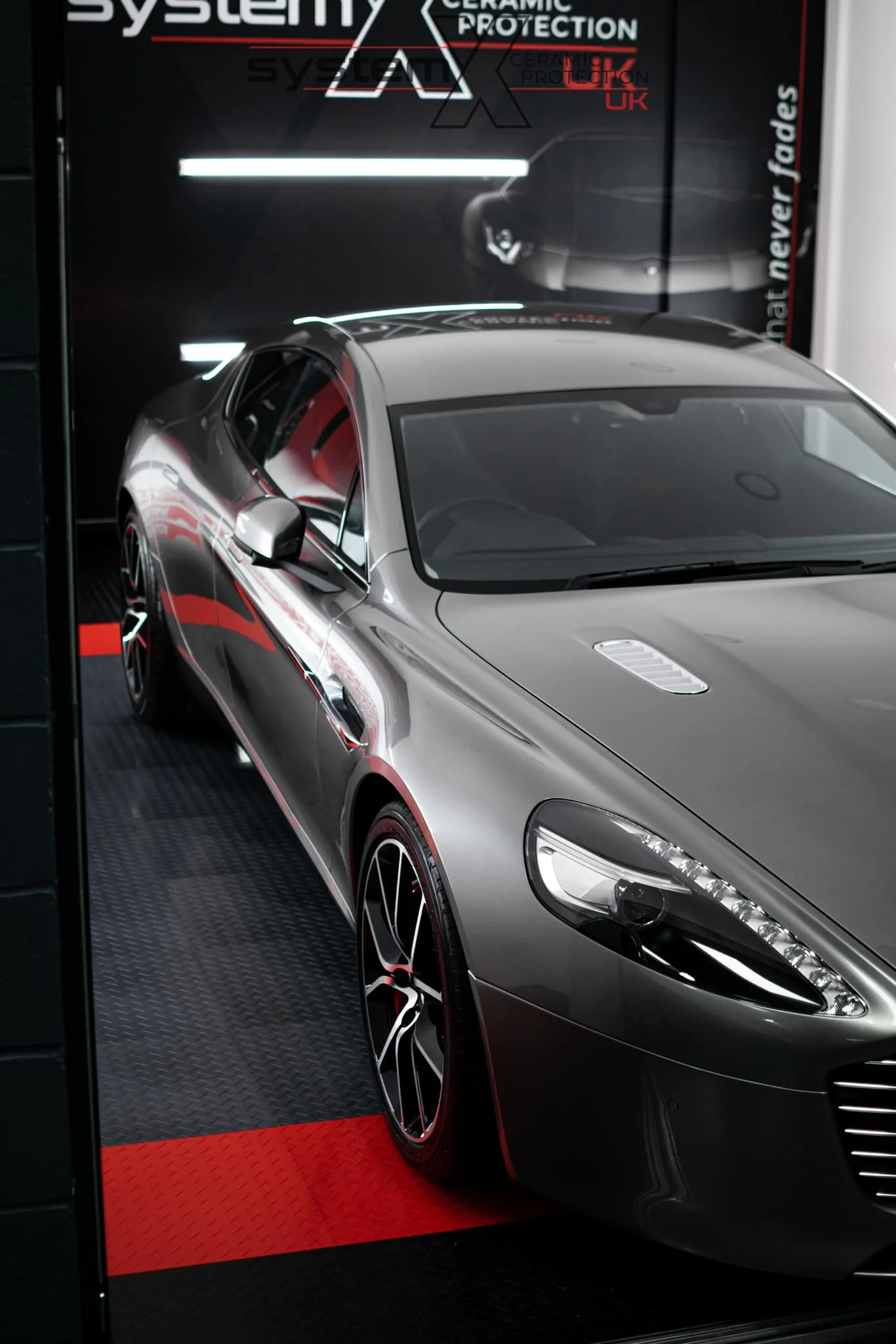 Silver Aston Martin Rapide with a System X ceramic coating, mirror-gloss finish reflecting the System X Ceramic Protection bay