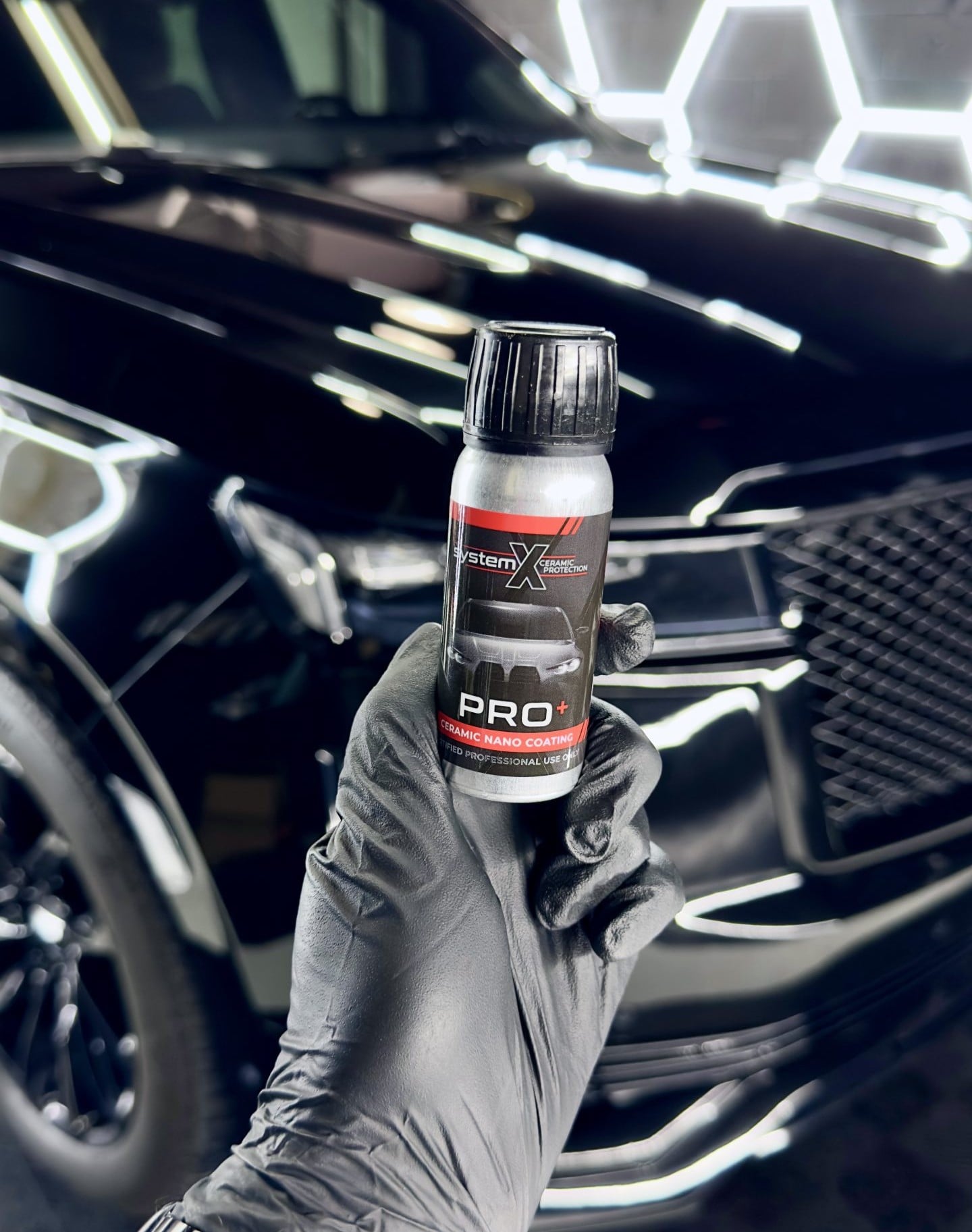 System X Certified installer holding a bottle of System X Pro+ ceramic coating in front of a freshly prepped black vehicle