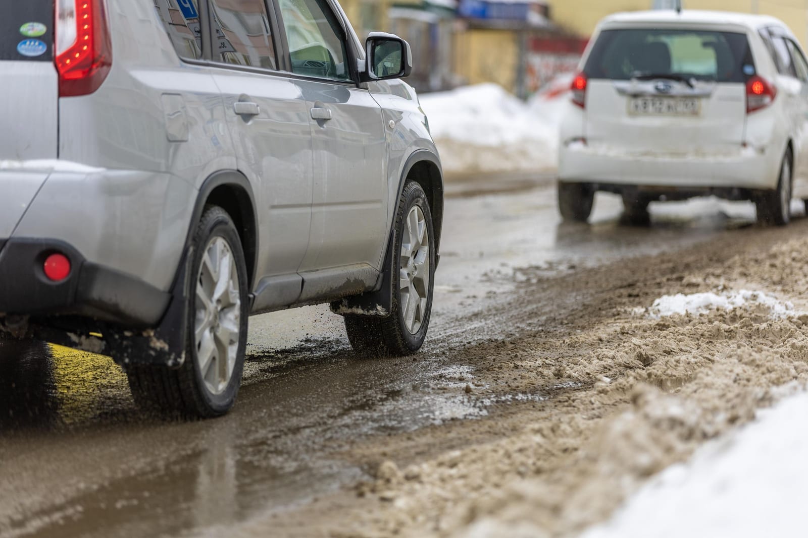 Cars driving through brown salt brine and slush on a treated winter road, grime thrown up over the lower doors and wheels