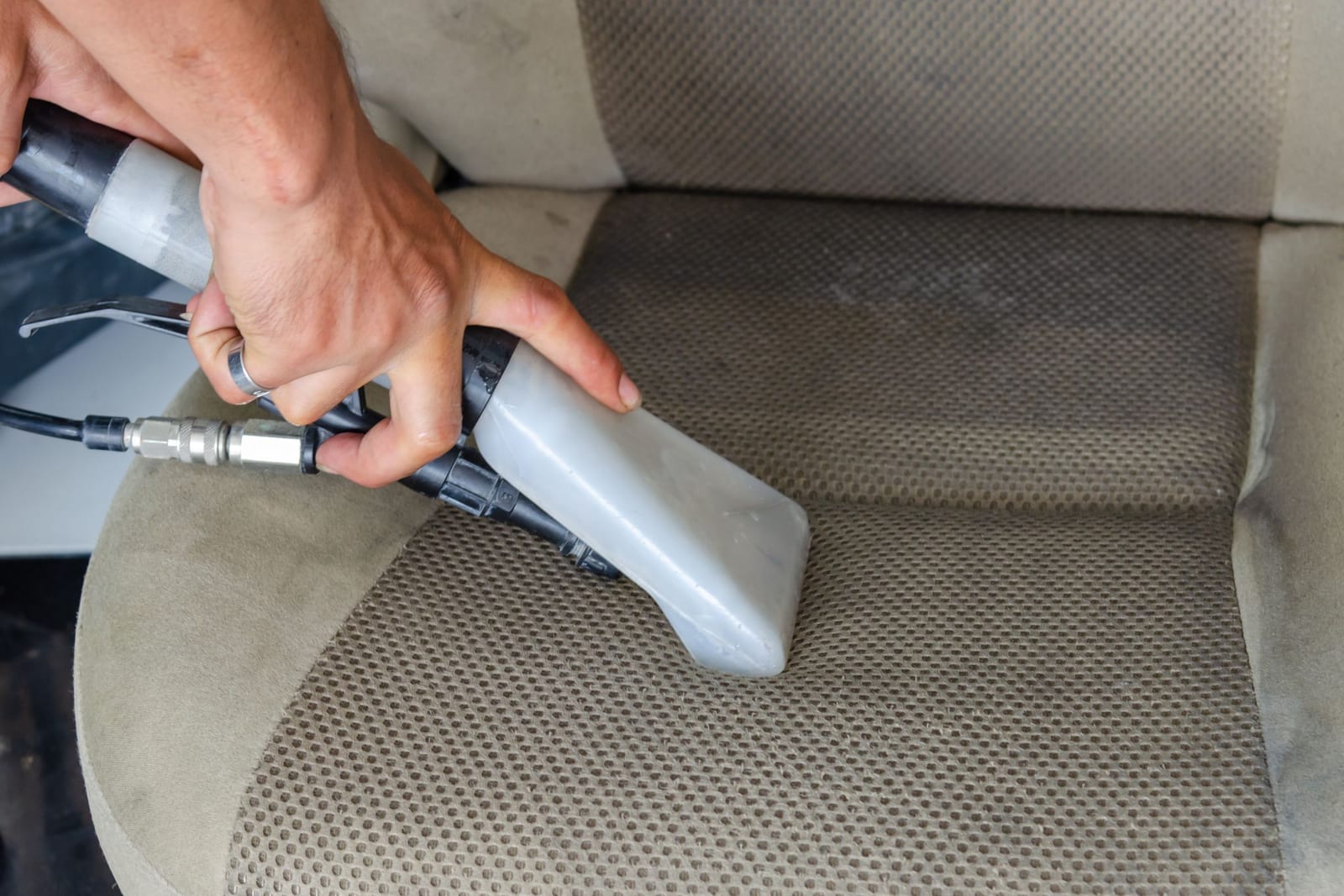 Hot-water extraction wand drawing a set-in stain out of a car's cloth seat, the cleaned strip visibly lighter than the fabric beside it