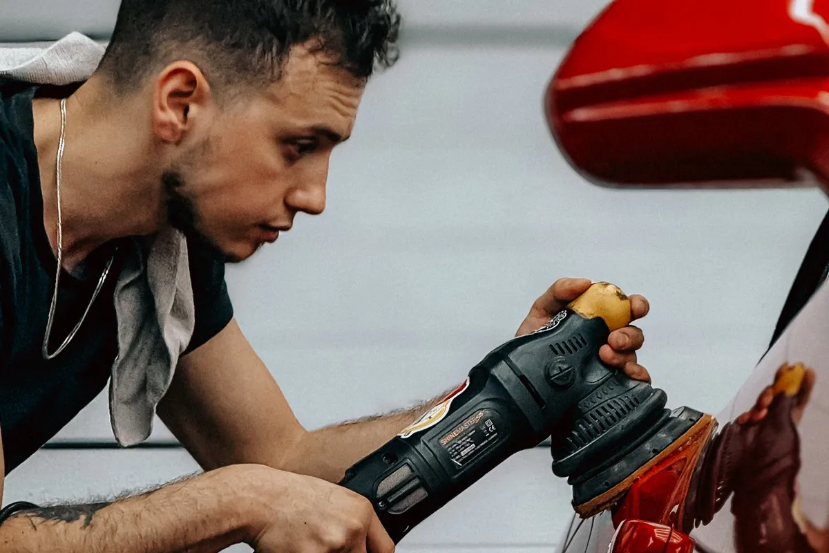 Detailing technician machine-polishing a red car's paint with a dual-action polisher at a Derry, NH auto detailing shop serving Salem drivers