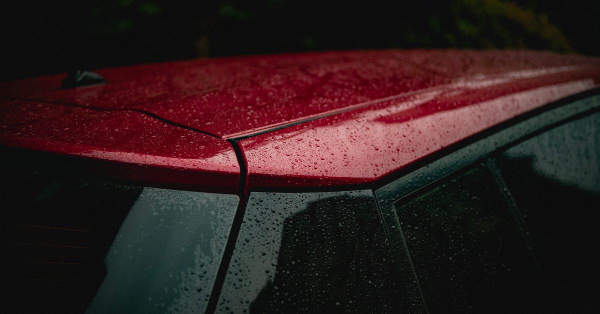 Raindrops beaded across the glossy red roof of a car above its rain-covered side windows