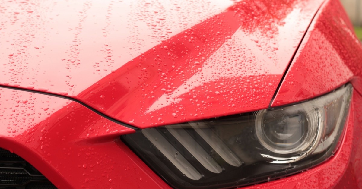 Rain beading on the glossy red hood and headlight of a new car