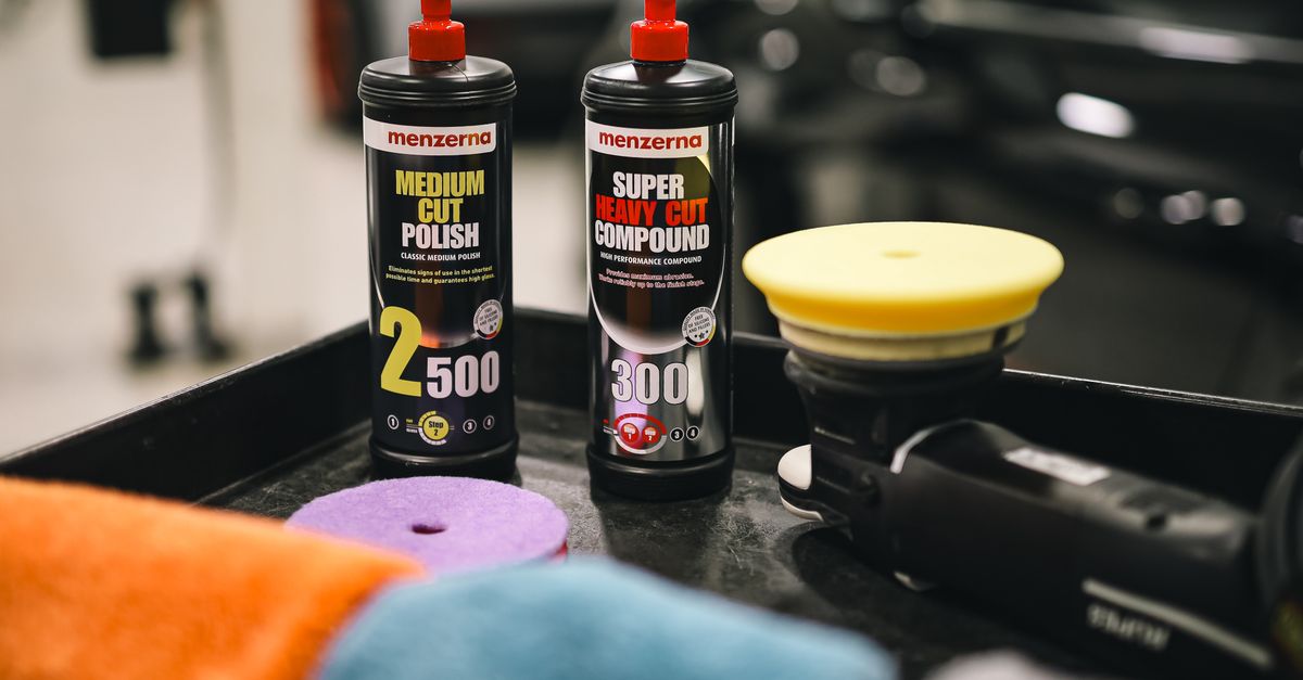 Bottles of heavy-cut compound and medium-cut polish beside a dual-action polisher and foam pads on a shop cart