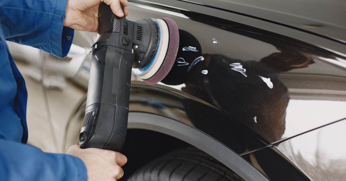 Detailer holding a dual-action polisher against the glossy black rear fender of a car dotted with polish